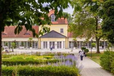 Gebäude mit rotem Dach und gelben Wänden, umgeben von Garten und Fußweg, vermutlich die Geschäftsstelle Debeka Heidenheim
