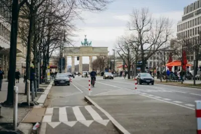 "Straße in Berlin mit Brandenburger Tor im Hintergrund, Autos und Radfahrer, Servicecenter AOK Nordost Gropiusstadt"