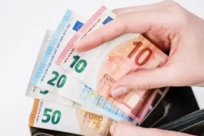 Hand hält Euro-Scheine aus einer schwarzen Geldbörse, Münzen und Banknoten in verschiedenen Wertstufen.