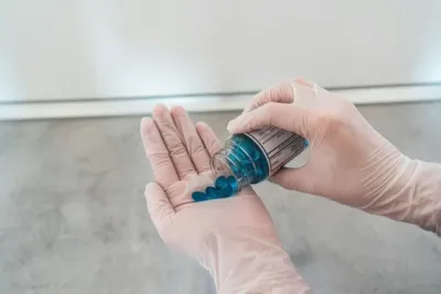 Ein Mitarbeiter im Gesundheitswesen hält eine Handvoll blauer Tabletten, während er eine Flasche öffnet.