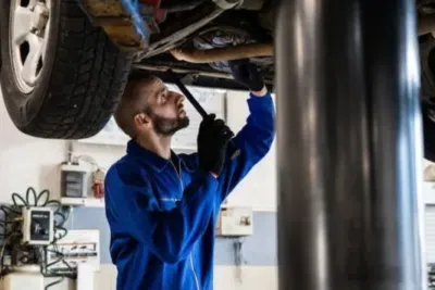 AOK vs Techniker Krankenkasse (TK) – Krankenkassen Vergleich 2026: Beitragssätze, Leistungen & Service im Detail 2 Ein Mechaniker in blauer Arbeitskleidung überprüft den Unterboden eines Autos in einer Werkstatt.